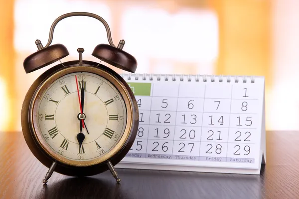 Reloj despertador y calendario sobre fondo brillante — Foto de Stock