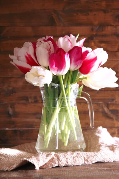 Schöne Tulpen im Glaskrug auf Holzgrund — Stockfoto