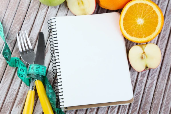 Cutlery tied with measuring tape and notebook with fruits on wooden background — Stock Photo, Image