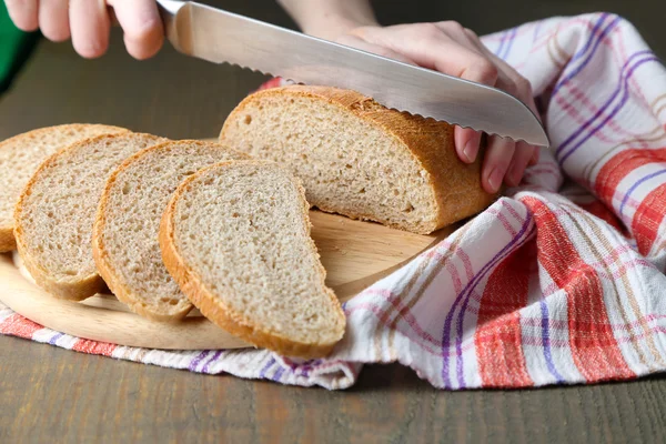 Mãos femininas cortando pão na placa de madeira, close-up — Fotografia de Stock