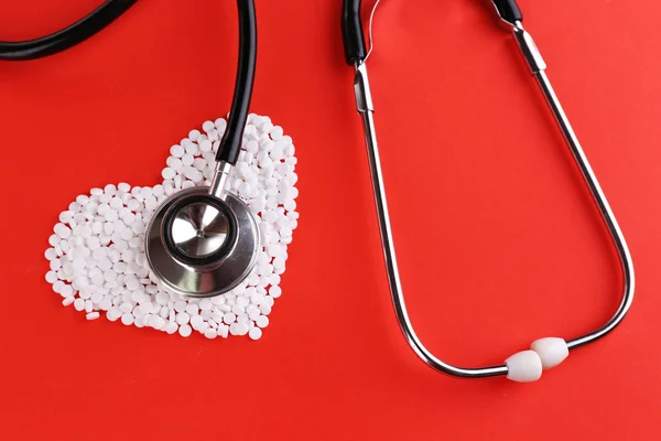 Pillen-Herz und Stethoskop auf rotem Hintergrund — Stockfoto