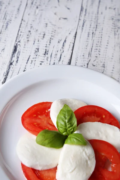 Caprese-Salat mit Mozarella, Tomaten und Basilikum auf Teller, auf Holztischhintergrund — Stockfoto