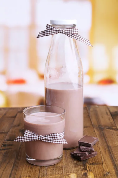 Chocolate milk in bottle and glass, on wooden table, on bright background — Stock Photo, Image