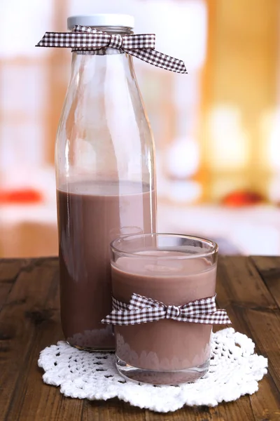 Suklaamaito pullossa ja lasissa, puupöydällä, kirkkaalla taustalla — kuvapankkivalokuva