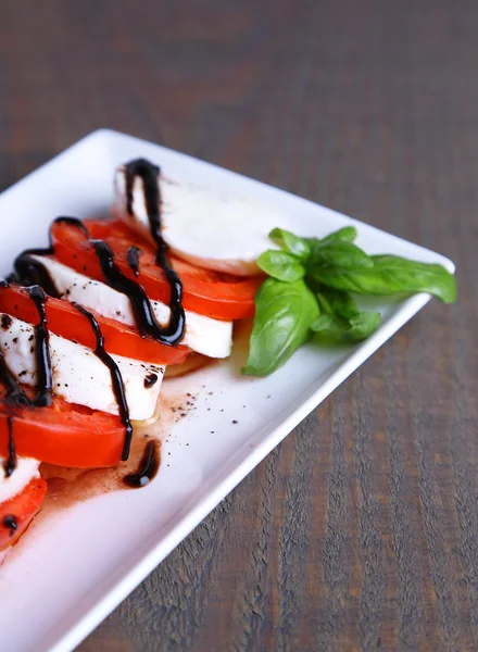 Caprese salade met mozarella kaas, tomaten en basilicum op plaat, op houten tafel achtergrond — Stockfoto