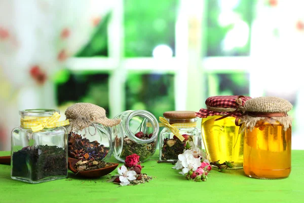 Assortiment d'herbes et thé et miel dans des bocaux en verre sur table en bois, sur fond lumineux — Photo