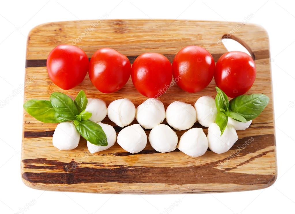 Tasty mozzarella cheese balls with basil and red tomatoes, on cutting board, isolated on white