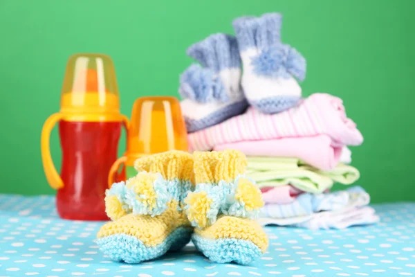 Composition with crocheted booties for baby, clothes and other things on color background — Stock Photo, Image