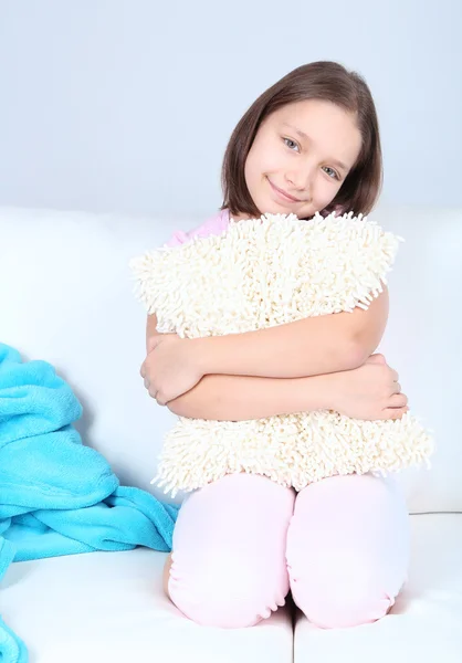 Красива маленька дівчинка сидить на дивані, на внутрішньому тлі будинку — стокове фото