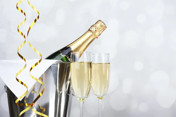 Glasses of champagne and bottle in pail on light background — Stock Photo, Image