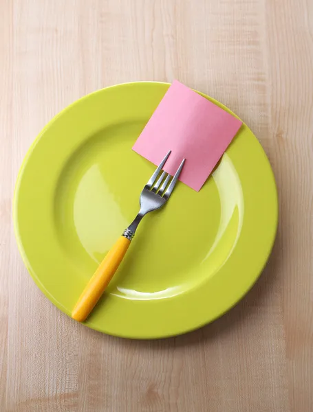 Empty note paper attached to fork, on plate, on color wooden background — Stock Photo, Image