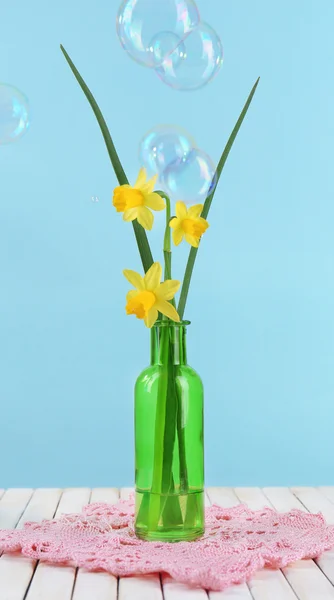 Beautiful irises and daffodils in bottle, on blue background — Stock Photo, Image