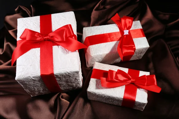 Schöne Geschenke mit roten Bändern auf seidenem Hintergrund — Stockfoto
