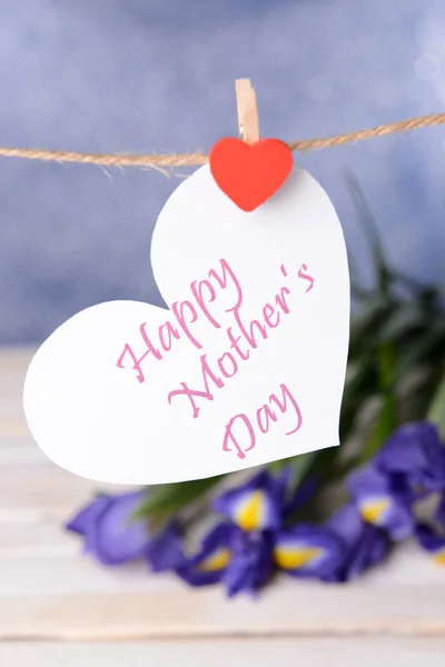 Happy Mothers Day message written on paper heart with flowers on purple background — Stock Photo, Image