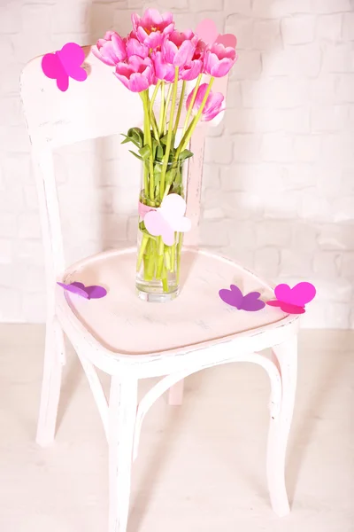 Composition with bouquet of tulips in vase, on chair, on wall background — Stock Photo, Image