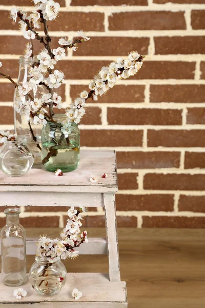 Beautiful apricot blossom in transparent jars on brick wall background — Stock Photo, Image