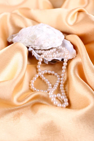 Wunderschöne Perlen in Muschel auf goldenem Seidentuch — Stockfoto