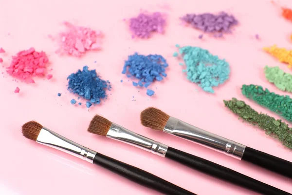 Rainbow krossade ögonskugga och professionella make-up pensel på rosa bakgrund — Stockfoto