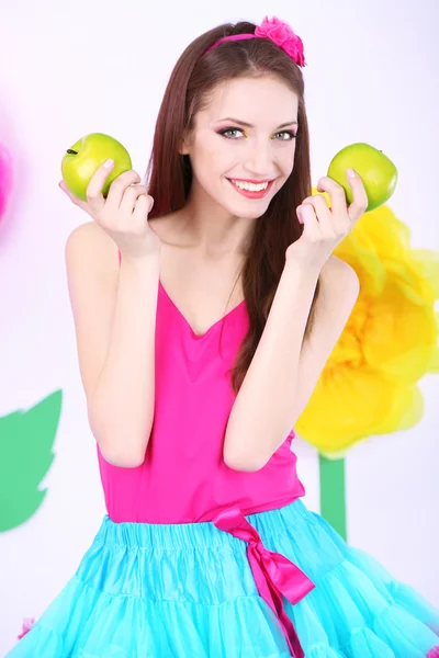 Hermosa joven en falda pequeña con manzanas sobre fondo decorativo —  Fotos de Stock