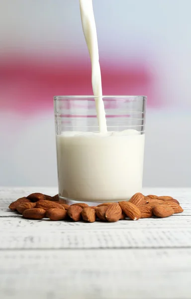 Mandelmilch wird in Glas gegossen, auf farbigem Holztisch, auf hellem Hintergrund — Stockfoto