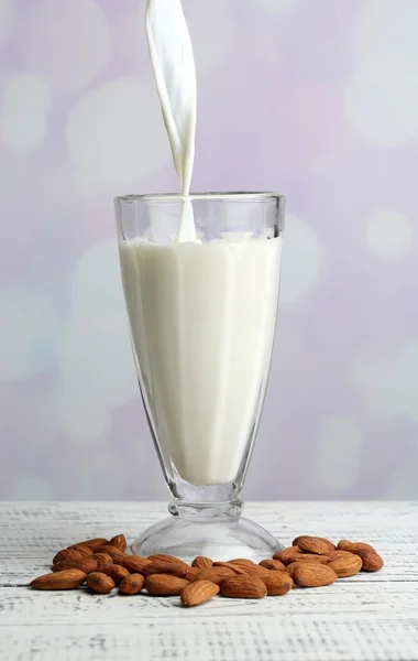 Миндальное молоко наливают в стекло, на цветной деревянный стол, на светлый фон — стоковое фото