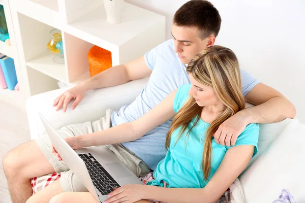 Coppia amorevole seduta con computer portatile sul divano, su sfondo interno di casa — Foto Stock
