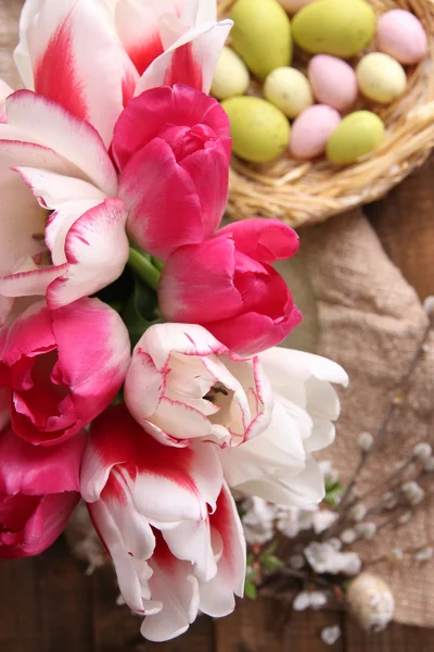 复活节彩蛋与美丽的郁金香，在木制的背景上的玻璃水罐组成 — 图库照片