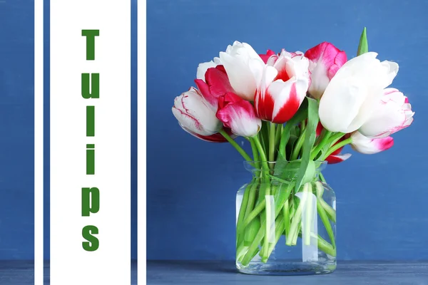 Beautiful tulips in glass jug on color wooden background — Stock Photo, Image