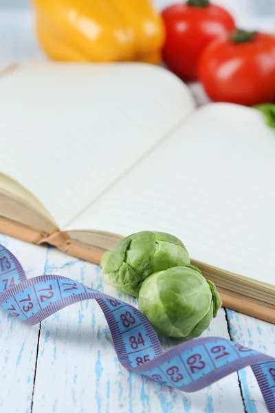 Book with measuring tape and vegetables on wooden background — Stock Photo, Image