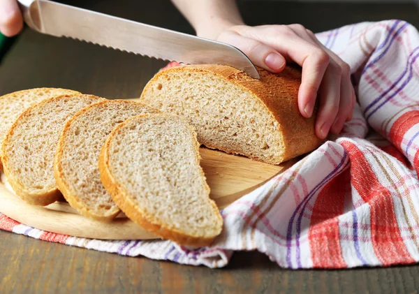 Mani femminili taglio del pane su tavola di legno, primo piano — Foto Stock