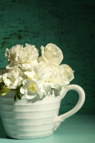 Beautiful spring flowers in cup on green background — Stock Photo, Image