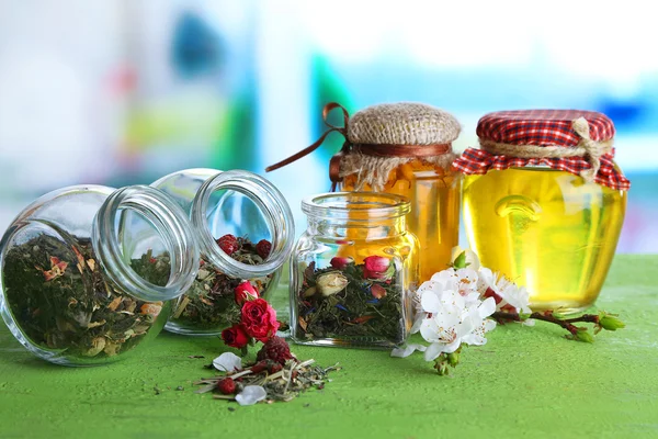 Assortment of herbs and tea in glass jars on wooden table, on bright background