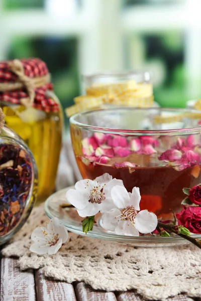 Assortimento di erbe aromatiche, tè e miele in barattoli di vetro e tazza di bevanda calda su tavolo di legno, su sfondo luminoso — Foto Stock