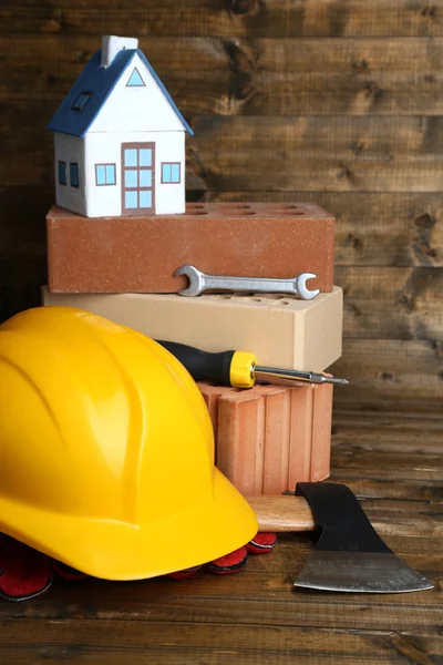 Composición con casco de seguridad, guantes de cuero, herramientas y casa decorativa sobre fondo de madera —  Fotos de Stock