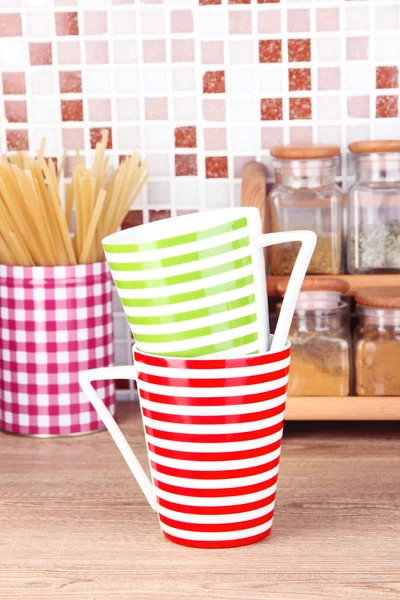 Cups in kitchen on table on mosaic tiles background — Stock Photo, Image