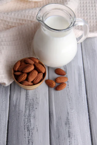Mandel mjölk i kannan med mandel i skål, på färg trä bakgrund — Stockfoto