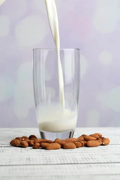 Mandlové mléko se nalije do sklenice, na barevný dřevěný stůl, na světlé pozadí — Stock fotografie