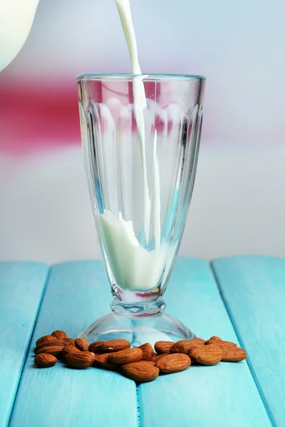 La leche de almendras se vierte en vidrio, sobre una mesa de madera de color, sobre un fondo claro — Foto de Stock