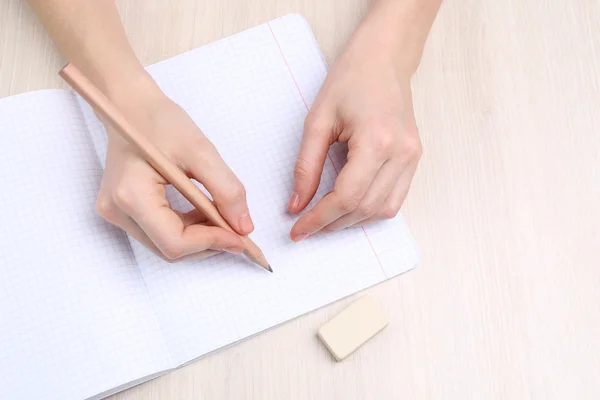 Manos humanas con lápiz escrito sobre papel y goma de borrar sobre fondo de mesa de madera — Foto de Stock