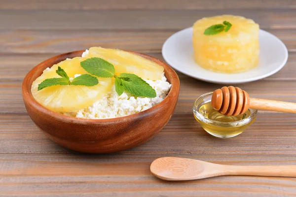 Bowl of tasty cottage cheese with pineapple on wooden table