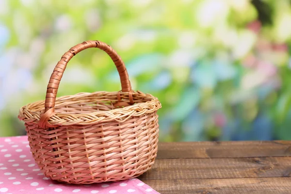 Empty wicker basket on wooden table, on bright background — Stock Photo, Image