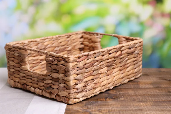 Empty wicker basket on wooden table, on bright background — Stock Photo, Image