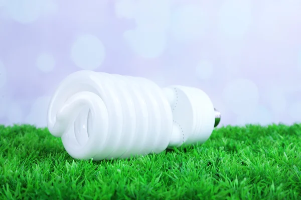 Energi menyimpan bola lampu di rumput hijau, pada latar belakang cahaya — Stok Foto