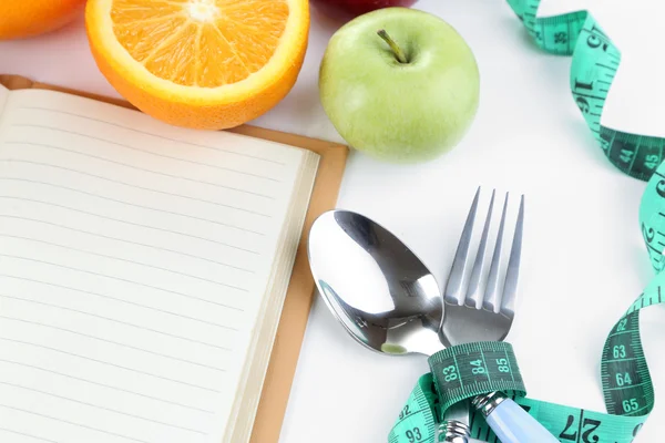 Talheres amarrados com fita métrica e livro com frutas de perto — Fotografia de Stock