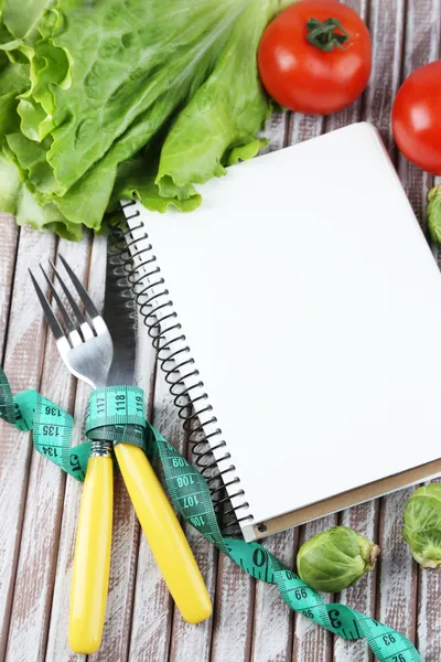 Bestick bundna med tejp och anteckningsboken med grönsaker på trä bakgrund — Stockfoto