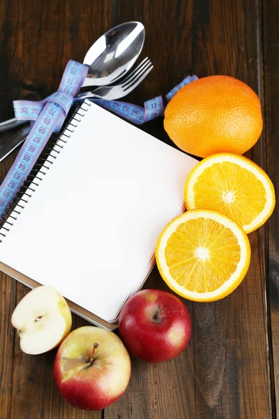Sztućce związany z pomiaru taśmę i notebook z owocami na drewniane tła — Zdjęcie stockowe