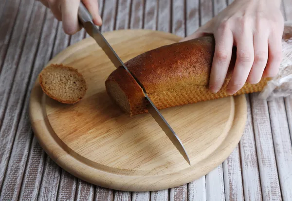 Manos femeninas cortando pan sobre tabla de madera, primer plano — Foto de Stock