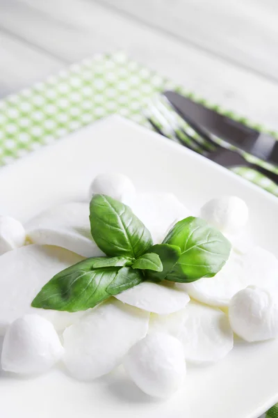 Sabroso queso mozzarella con albahaca en plato sobre fondo de madera — Foto de Stock