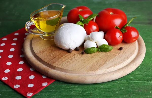 Lezzetli mozzarella Peynirli cips, fesleğen ve kırmızı domates, renk ahşap zemin üzerinde kesme tahtası üzerine zeytinyağı ile kompozisyon — Stok fotoğraf