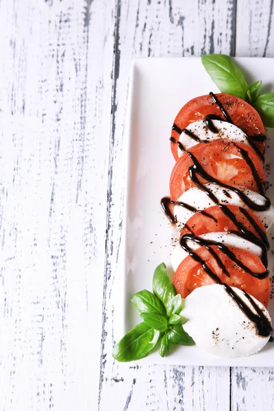 Caprese-Salat mit Mozarella, Tomaten und Basilikum auf Teller, auf Serviette, auf Holztischhintergrund — Stockfoto